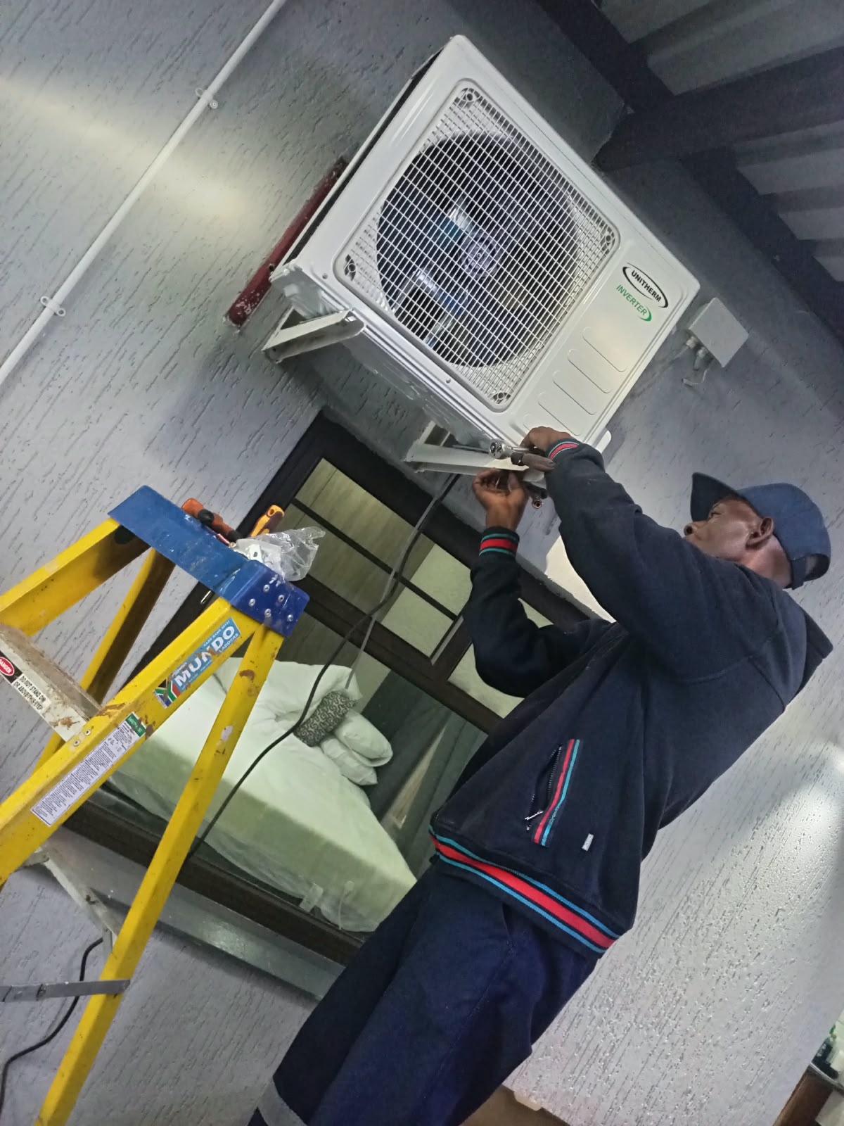 Technician on a ladder installing a wall-mounted aircon unit