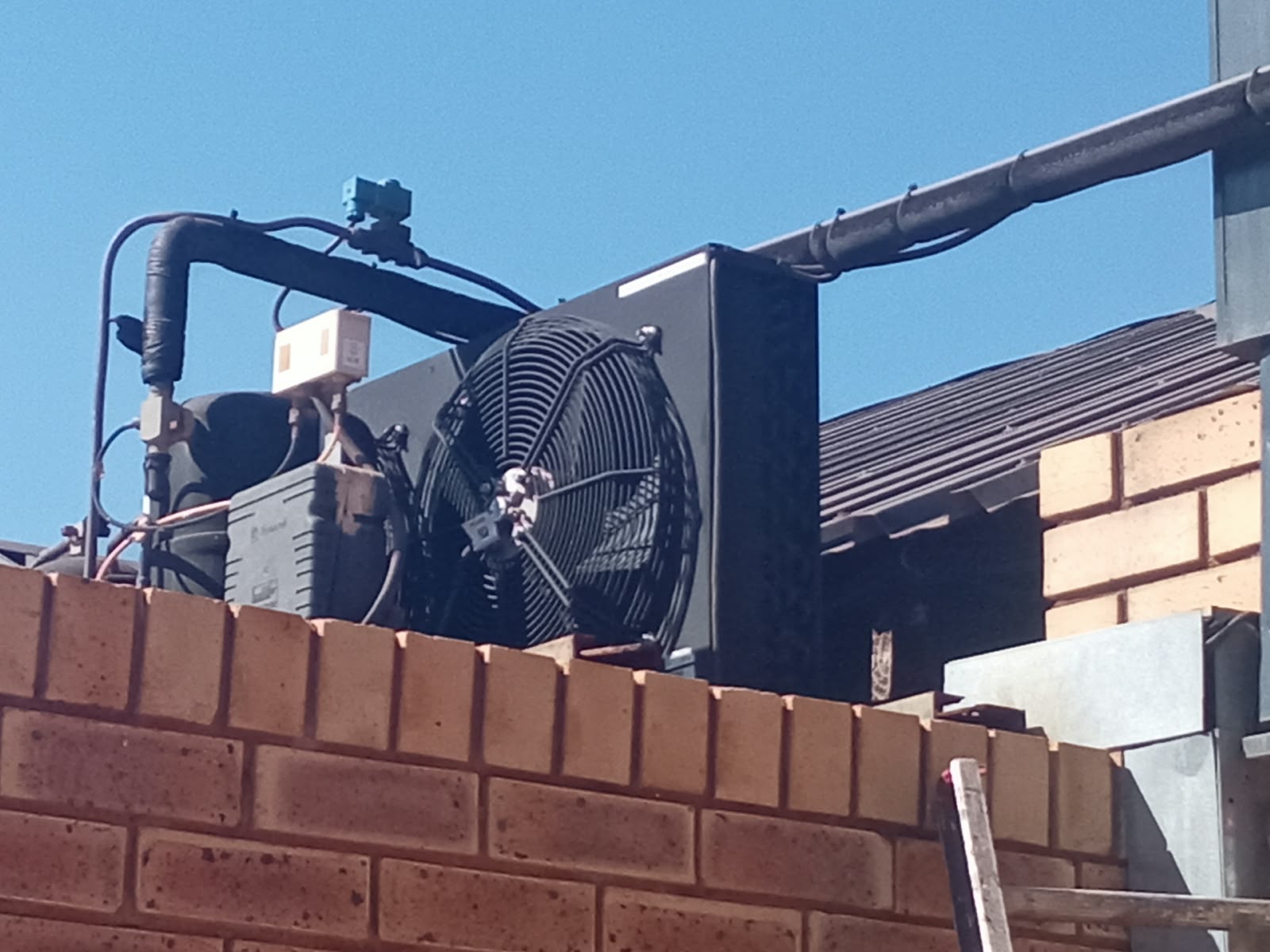 Large industrial condenser fan unit above a brick wall